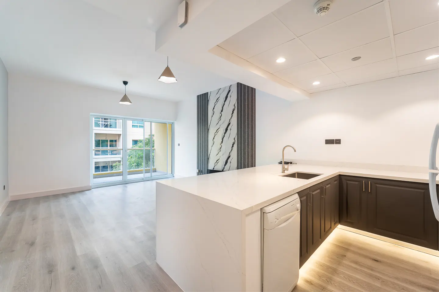 Bright, modern kitchen with white countertops, dark cabinets, and stainless steel sink. Sliding glass doors lead to a balcony.