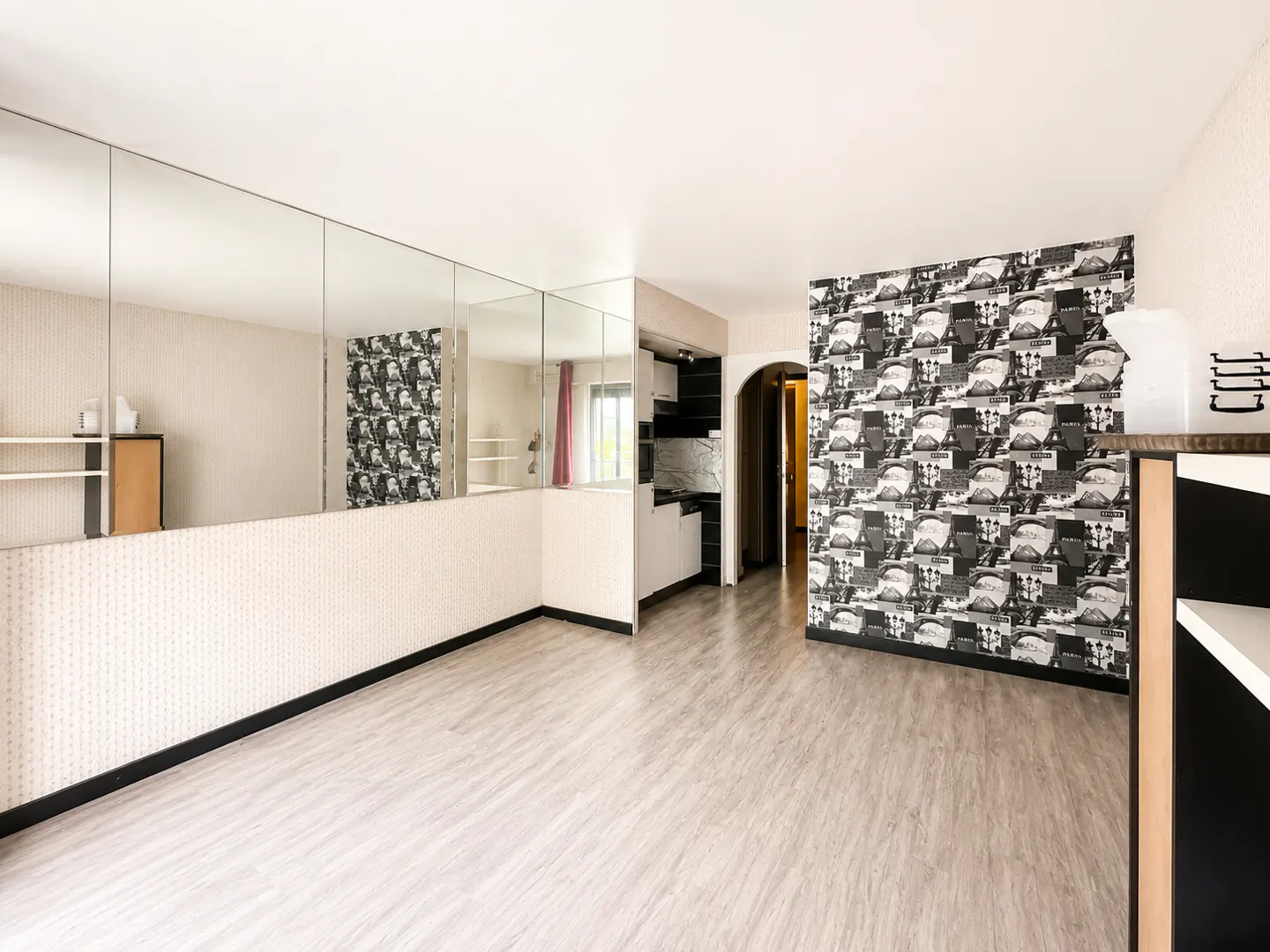 Bright room with light wood floors, a mirrored wall, and an accent wall featuring black and white Parisian-themed wallpaper.