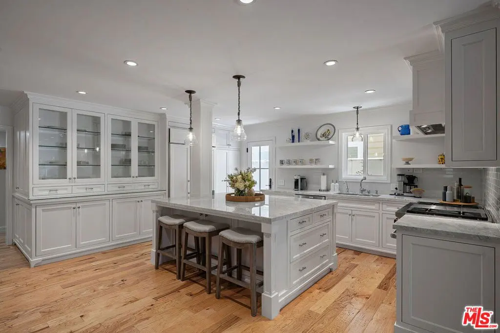 Bright, white kitchen with wood floors, island with stools, and glass-front cabinets.