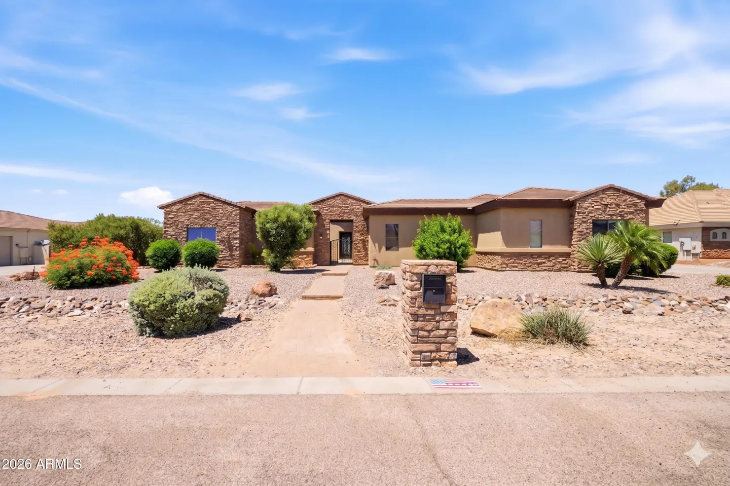 Single-story desert home with stone facade, xeriscaped front yard, and a stone mailbox under a bright blue sky.