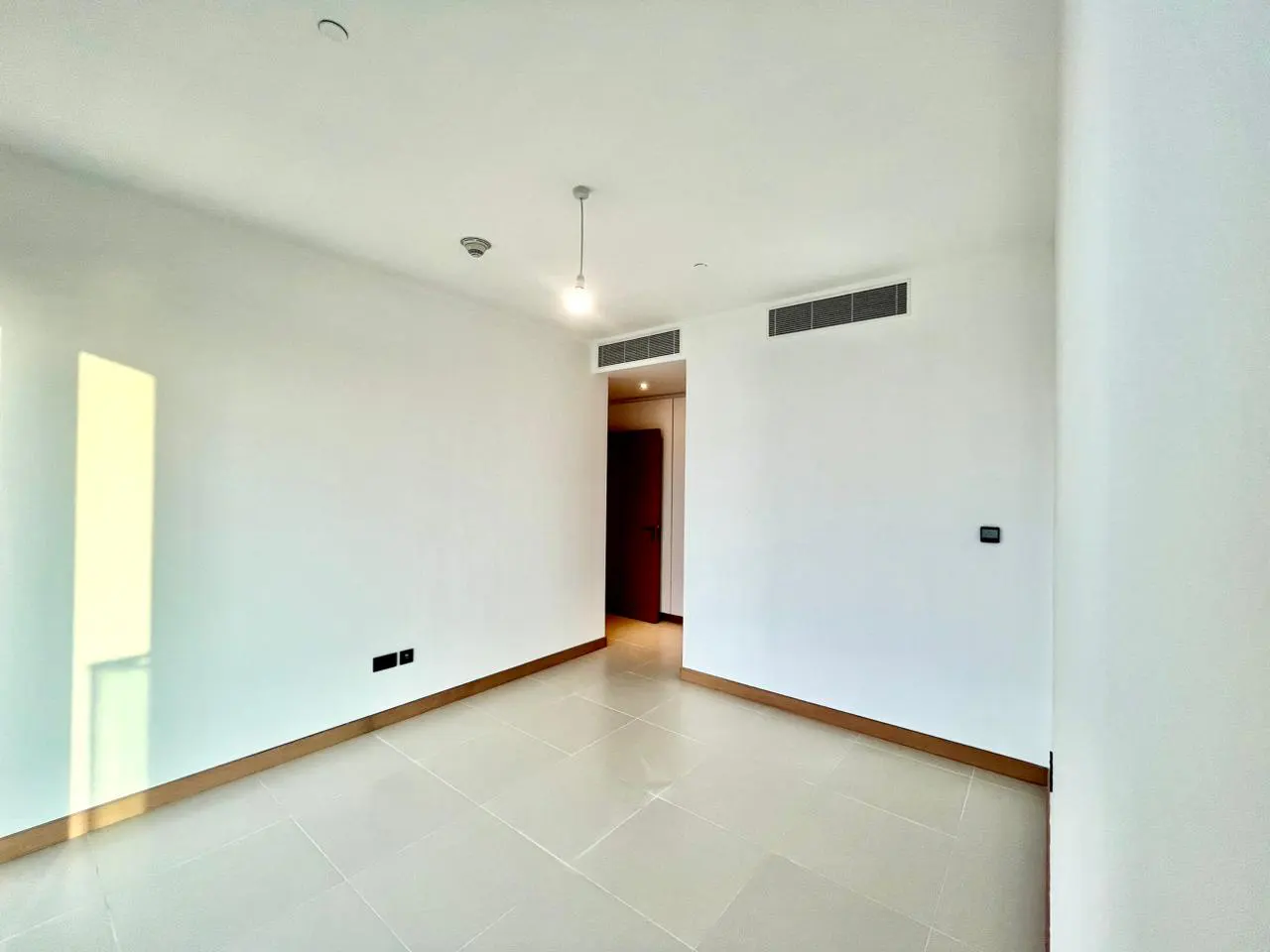 Empty room with white walls, beige tile floor, and a doorway leading to another room.