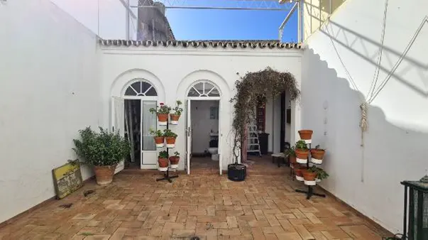A courtyard with brick flooring, white walls, arched doorways, and potted plants.