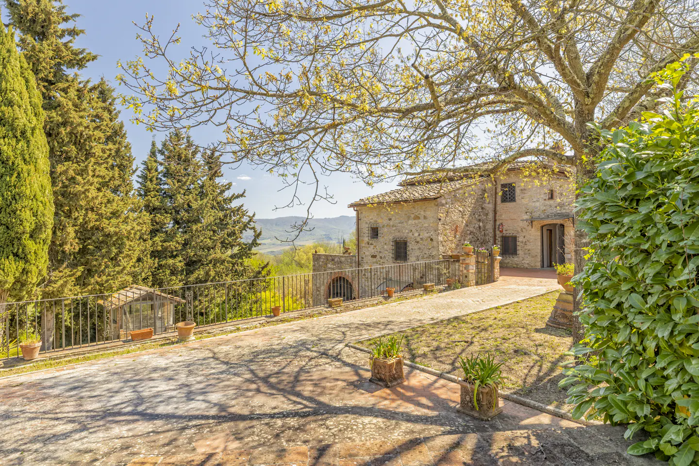 Exterior view of a stone Tuscan villa with a tiled roof, surrounded by trees and greenery on a sunny day.