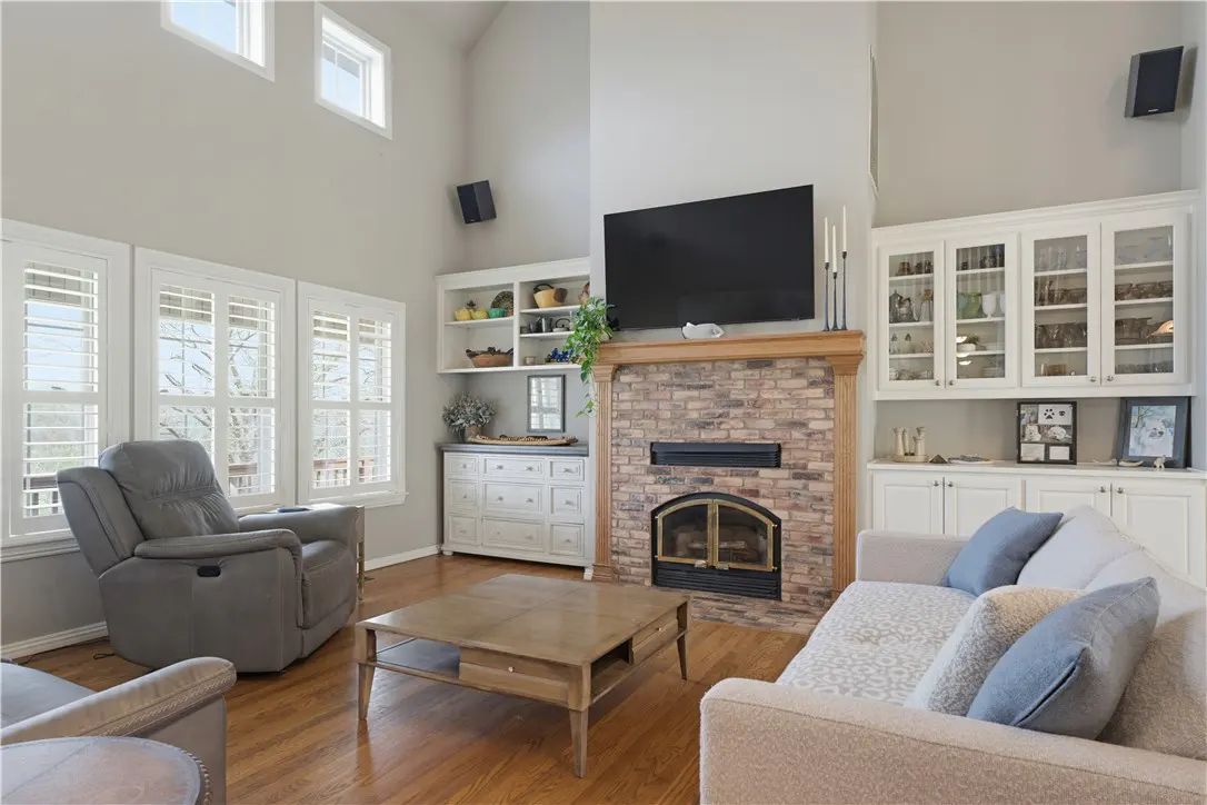 Living room with hardwood floors, gray walls, and a brick fireplace. A gray recliner sits near windows, and a beige sofa faces the fireplace.