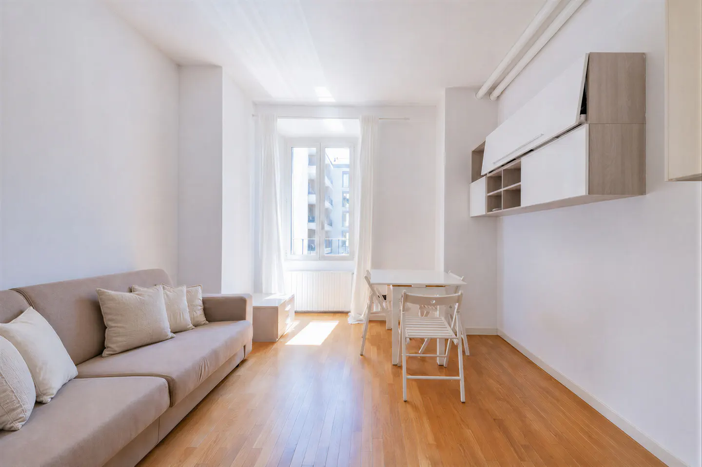 Bright living room with a beige sofa, white dining set, wooden floors, and modern wall-mounted storage cabinets.