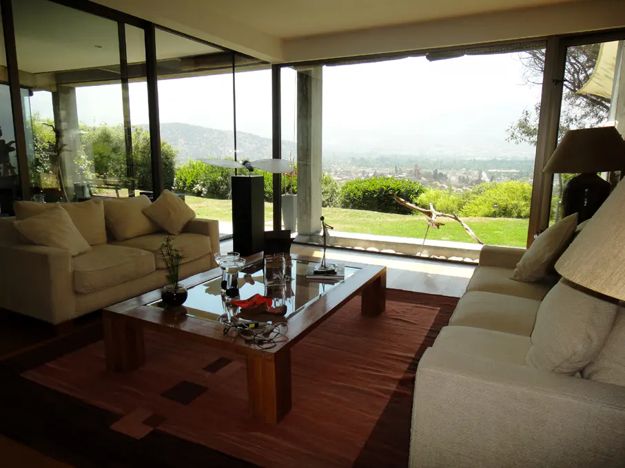 Bright living room with beige sofas, a wood and glass coffee table, and floor-to-ceiling windows overlooking a green landscape.