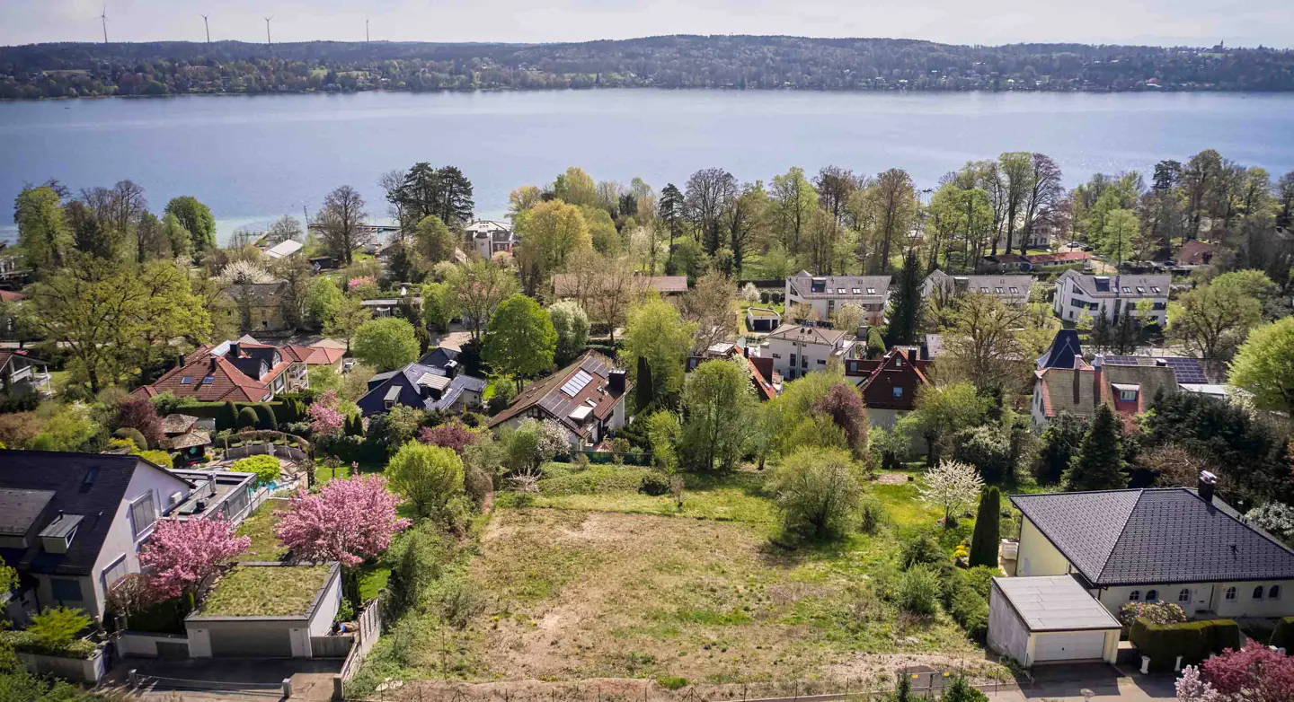 Aerial view of a vacant lot surrounded by houses and trees, with a lake in the background.