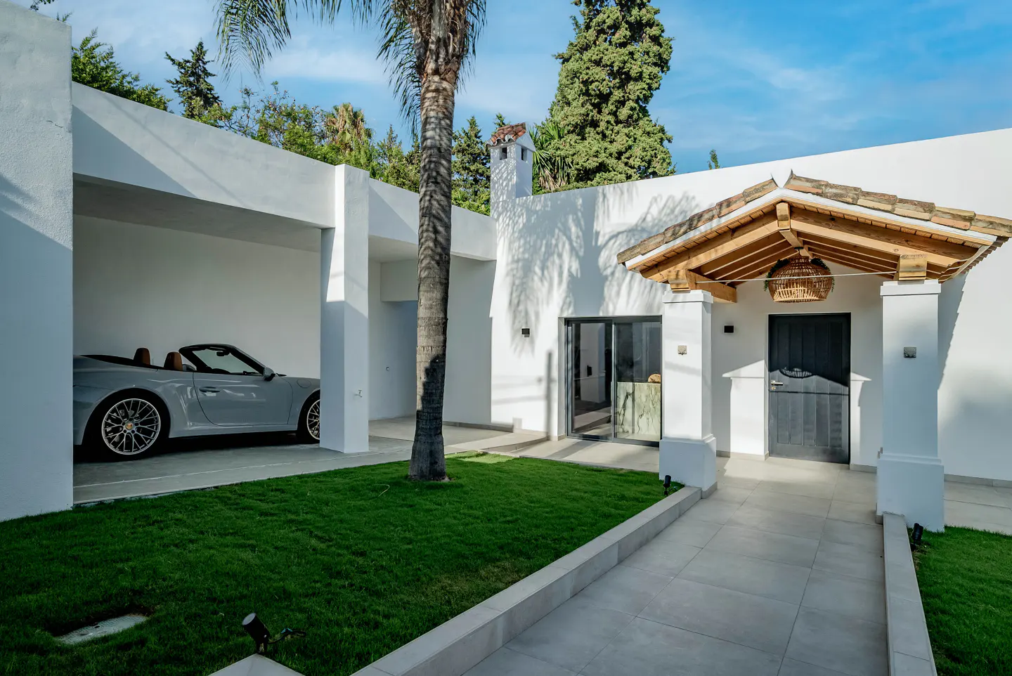 Modern white house exterior with a gray convertible in the garage, green lawn, and a covered entrance with a dark door.