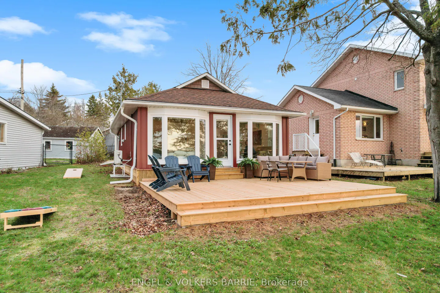 Exterior view of a red and white house with a wooden deck, chairs, and outdoor furniture on a grassy lawn.