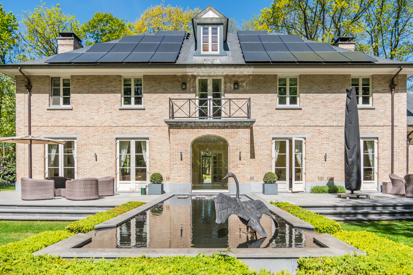 Exterior of a two-story brick house with solar panels, a water feature, and a swan statue.