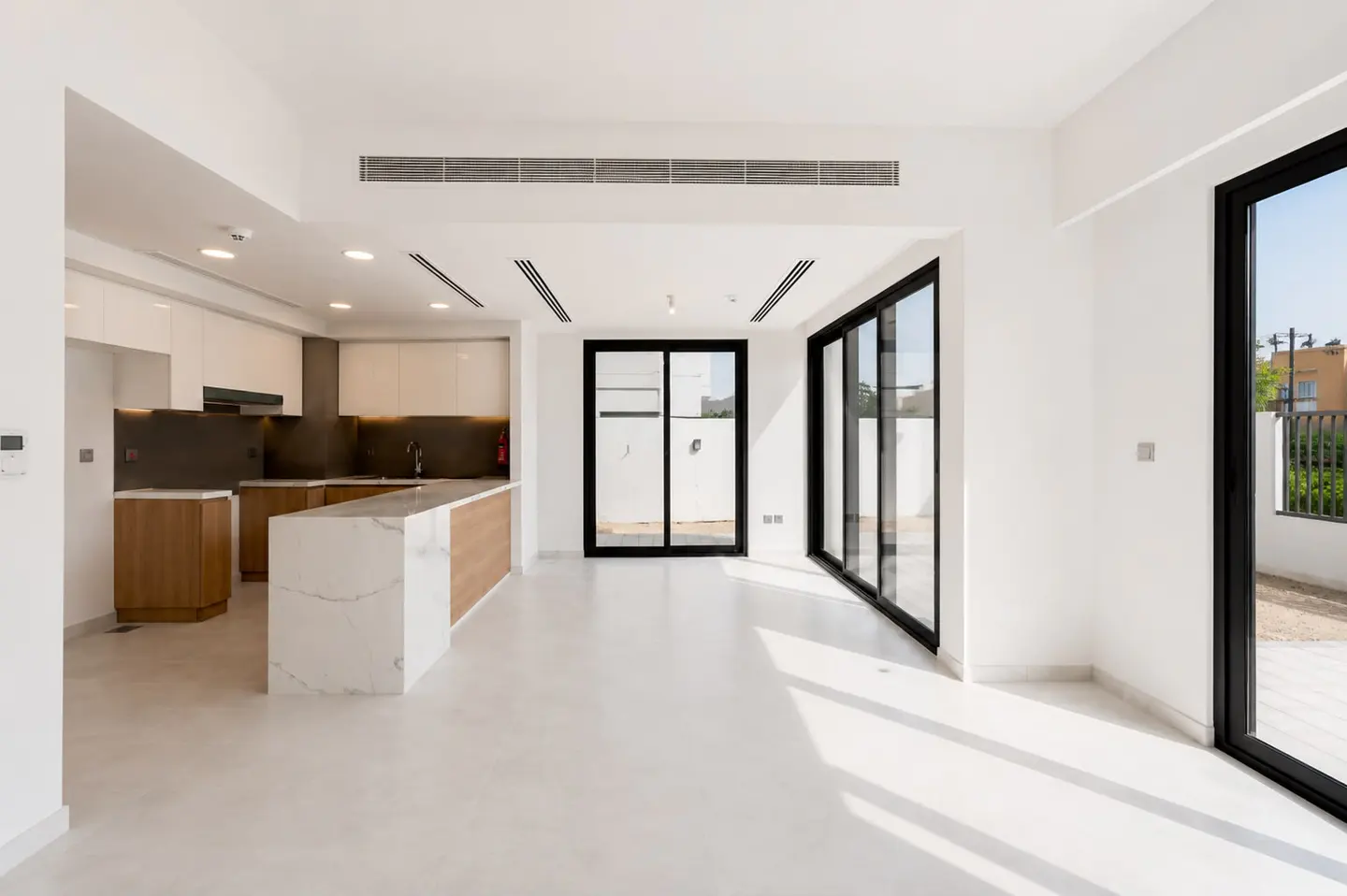 Modern open-plan kitchen with white marble island, wood cabinets, and large glass sliding doors leading to a patio.