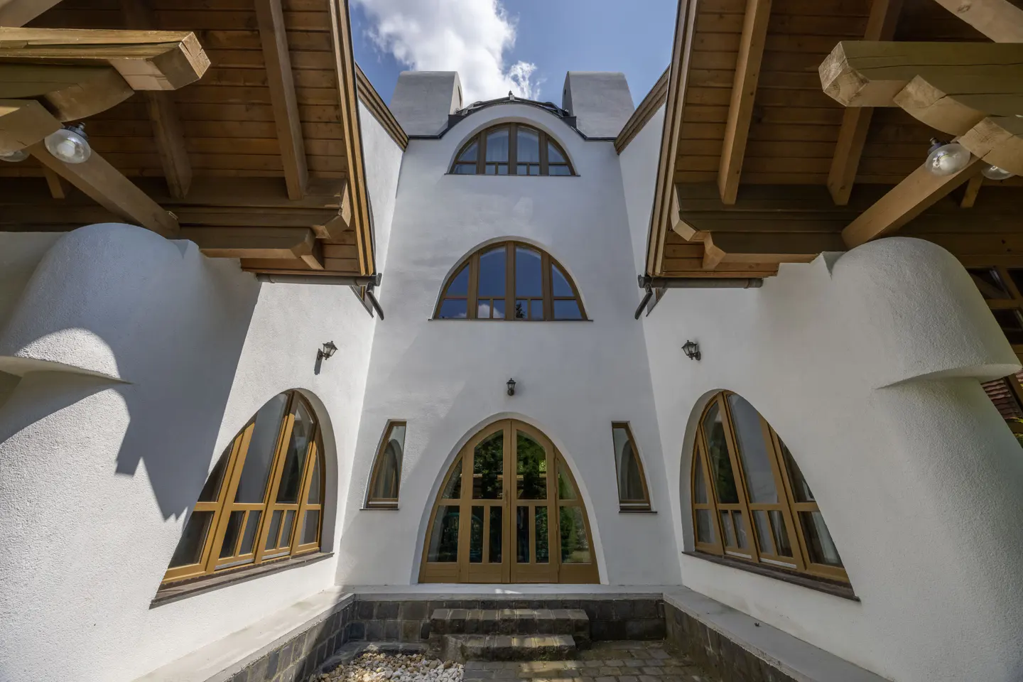 Exterior of a white stucco house with arched windows and wooden beams under a blue sky.