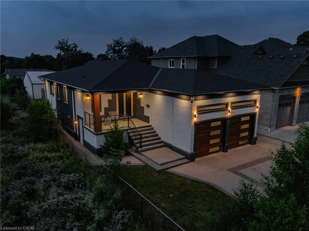 Exterior shot of a modern two-story home with a black roof, white walls, and a two-car garage with wood doors at dusk.