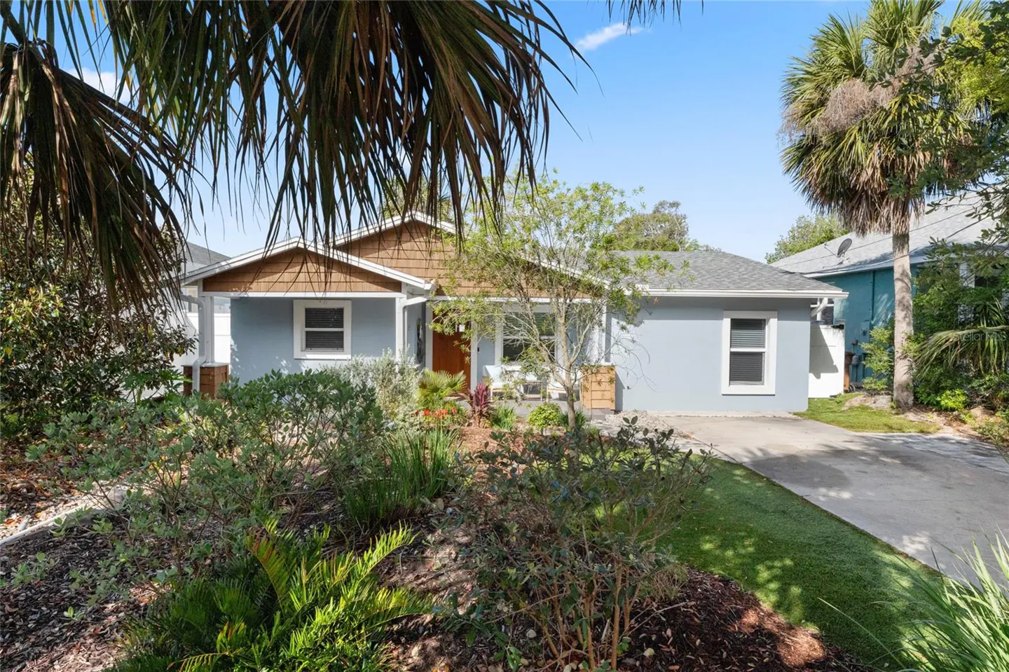 Front view of a light blue house with brown trim and a well-manicured lawn. Palm trees frame the house.
