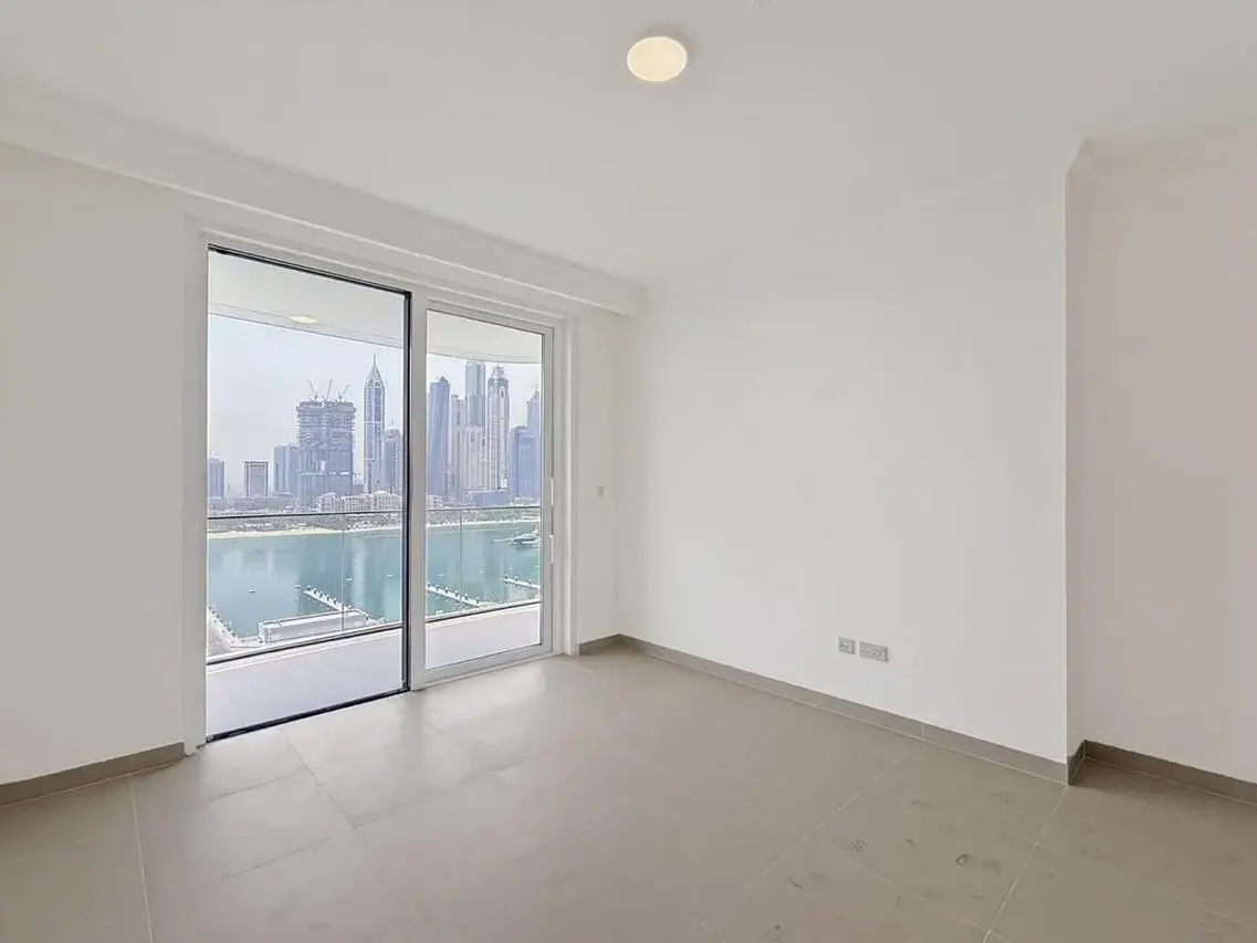 Empty room with gray tile floor, white walls, and sliding glass doors to a balcony overlooking a city skyline and water.
