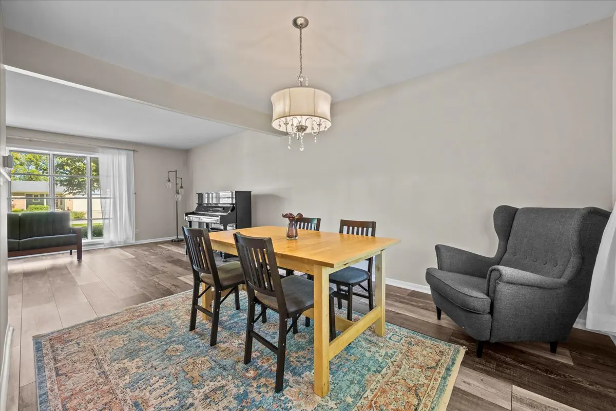 Dining area with a wooden table, four black chairs, a grey armchair, and a chandelier over a blue patterned area rug.