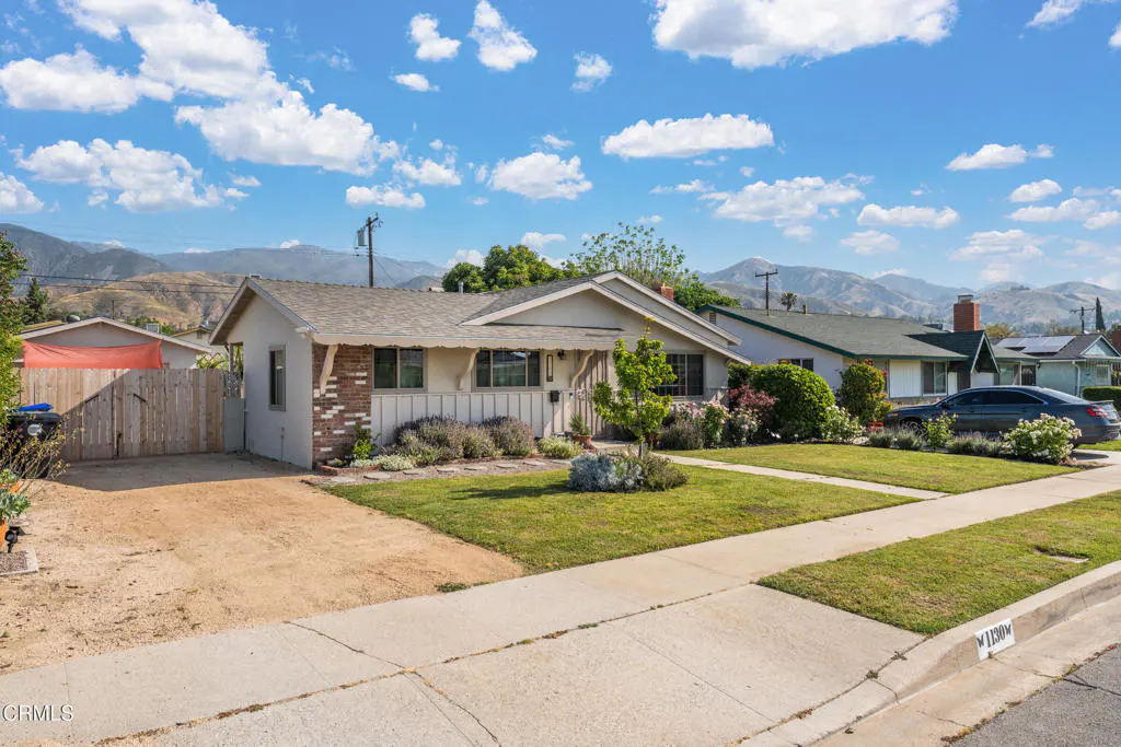 A single-story house with a lawn, brick accents, and mountains in the background under a blue, cloudy sky.