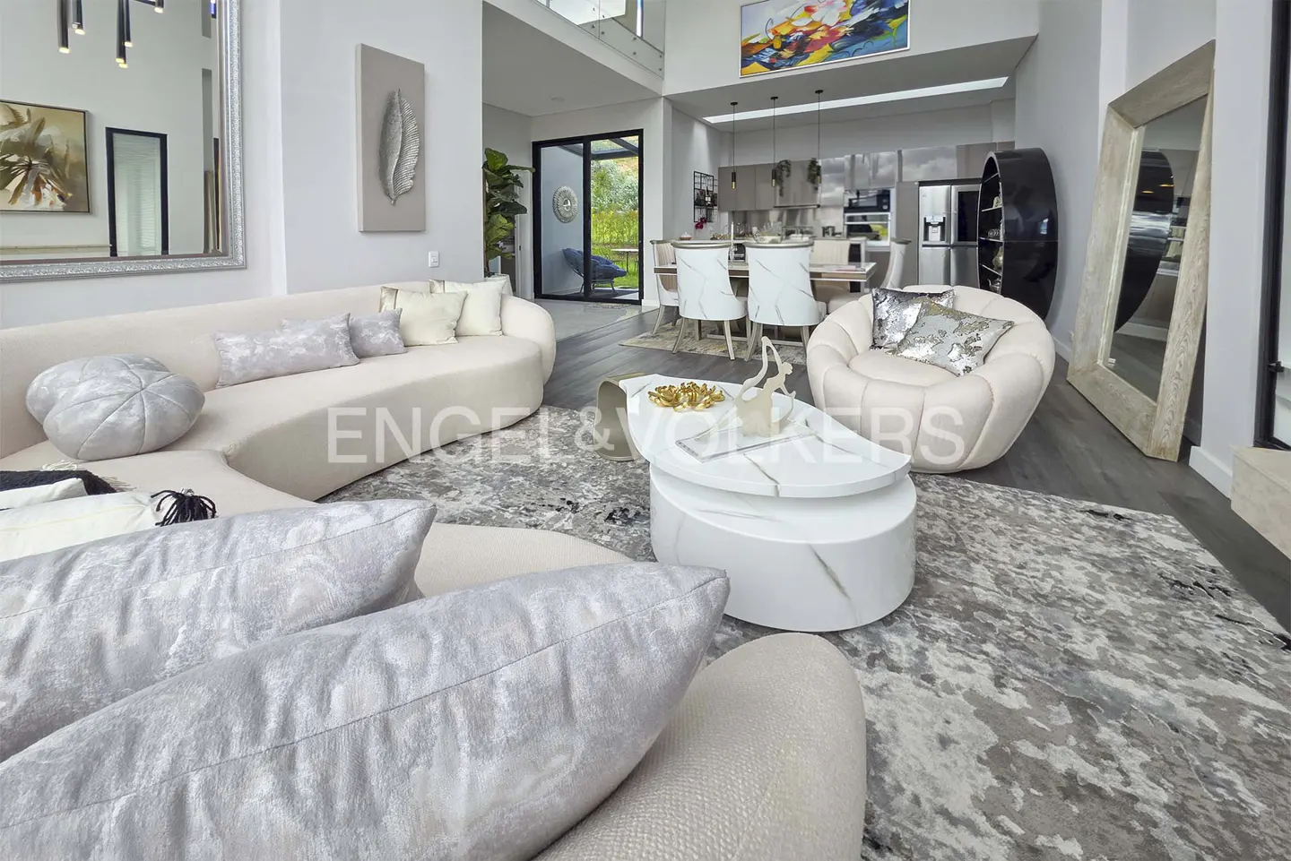 A modern living room with a curved beige sofa, white marble coffee table, and a gray patterned rug.