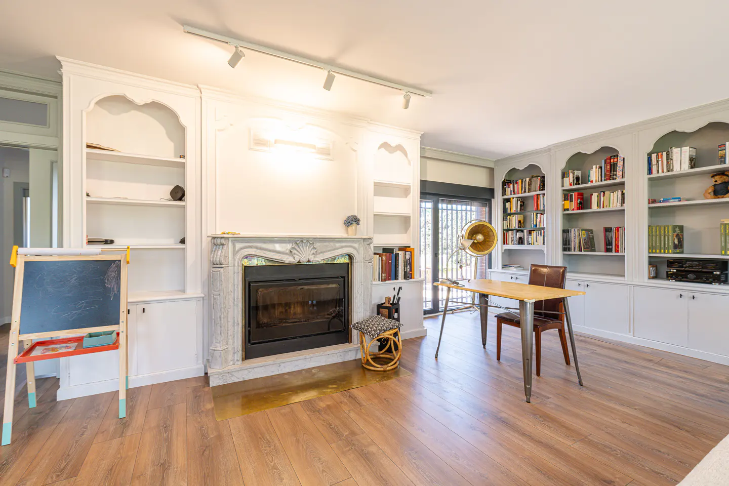 Living room with wood floors, white built-in shelves, fireplace, desk, and chalkboard.