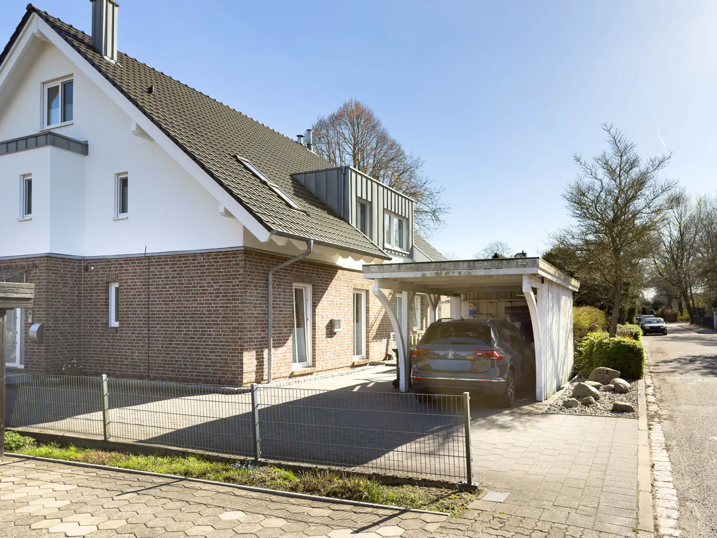 Two-story house with brick and white siding, a carport with a car, and a gray metal fence.