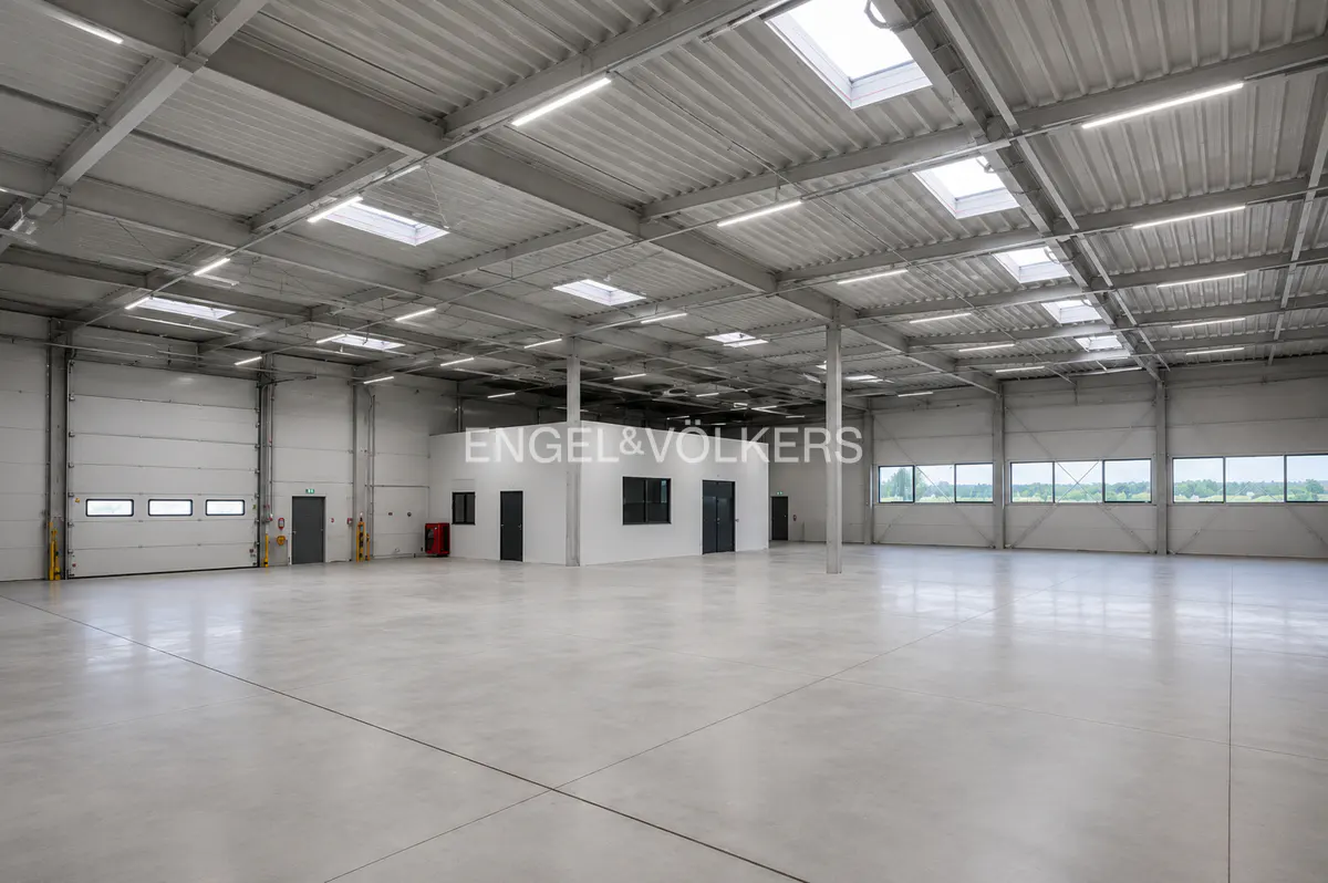Spacious, empty industrial warehouse with a polished concrete floor, high ceilings, skylights, and a central office block.