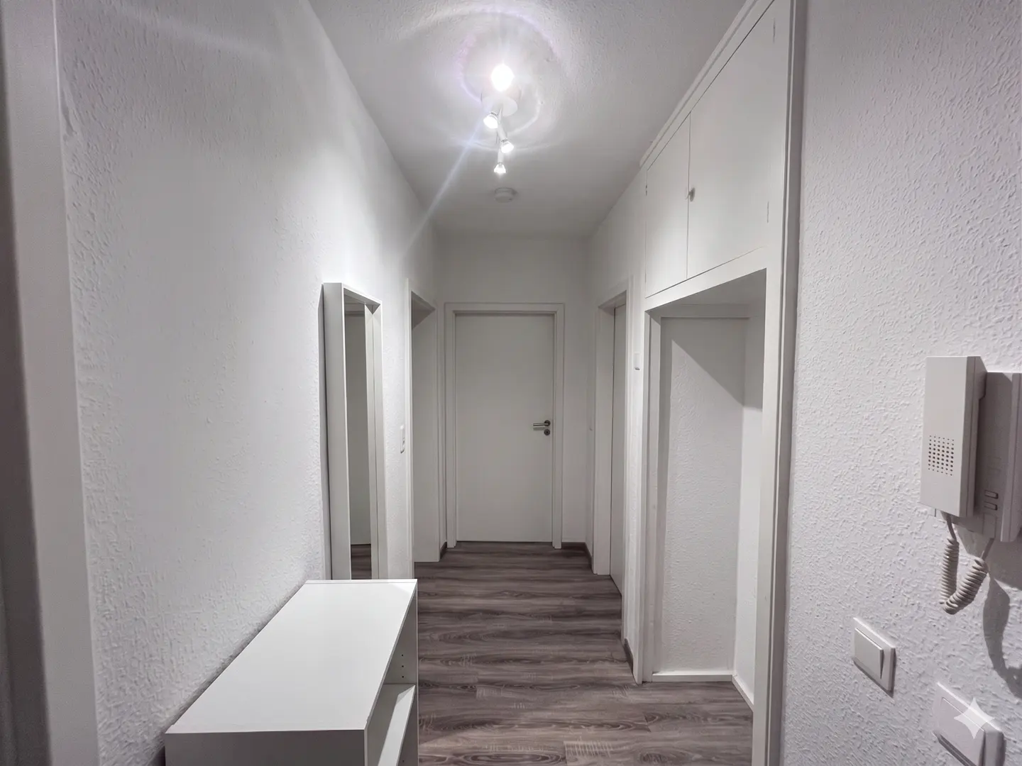 A bright hallway with white walls, doors, and trim, featuring a console table, mirror, and wood-look flooring.