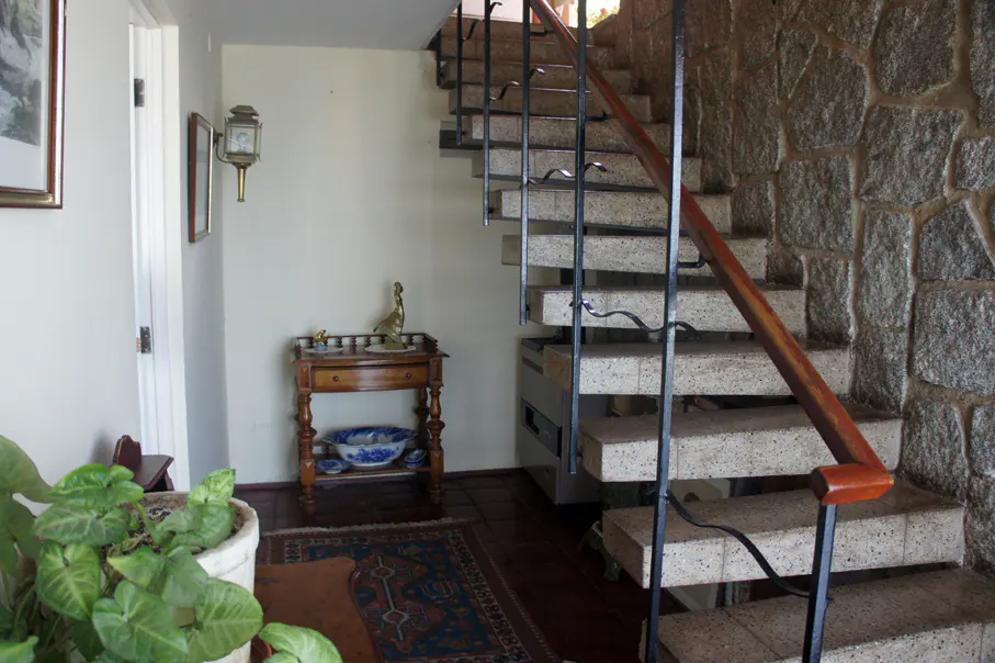 Interior view of a home's foyer with stone wall, staircase with black railing, and a small wooden table with a blue and white bowl.