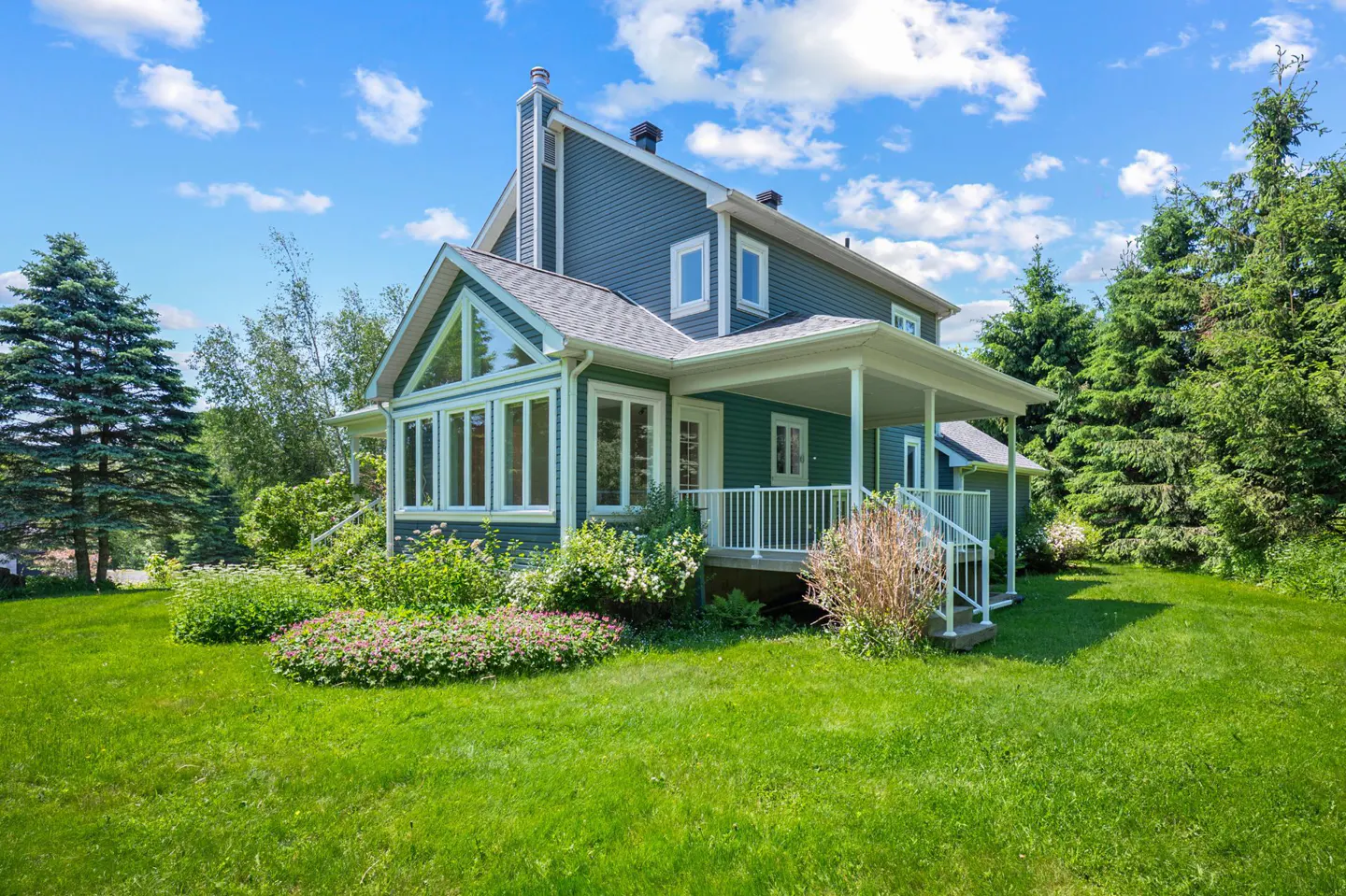 Blue two-story house with a covered porch, large windows, and a lush green lawn under a bright blue sky.