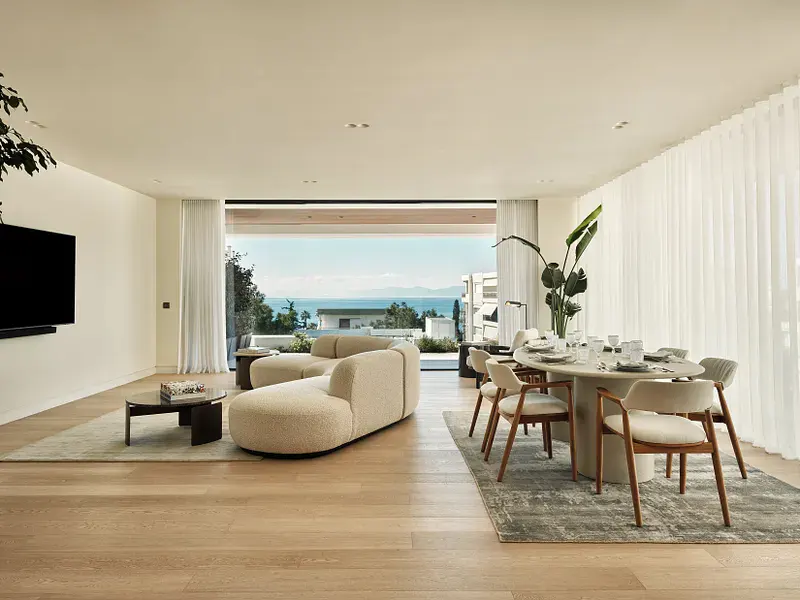 Bright, open-plan living space with a cream sofa, round dining table, and ocean view through large windows.