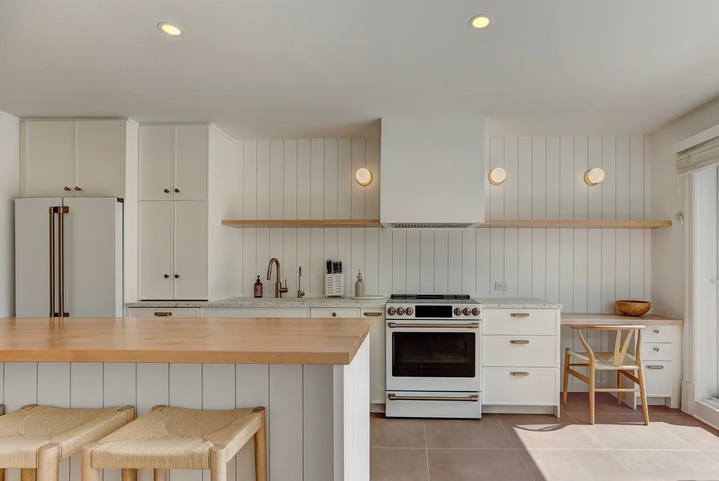 Bright, modern kitchen with white cabinets, wood island, and stainless steel appliances. Two woven stools sit at the island.