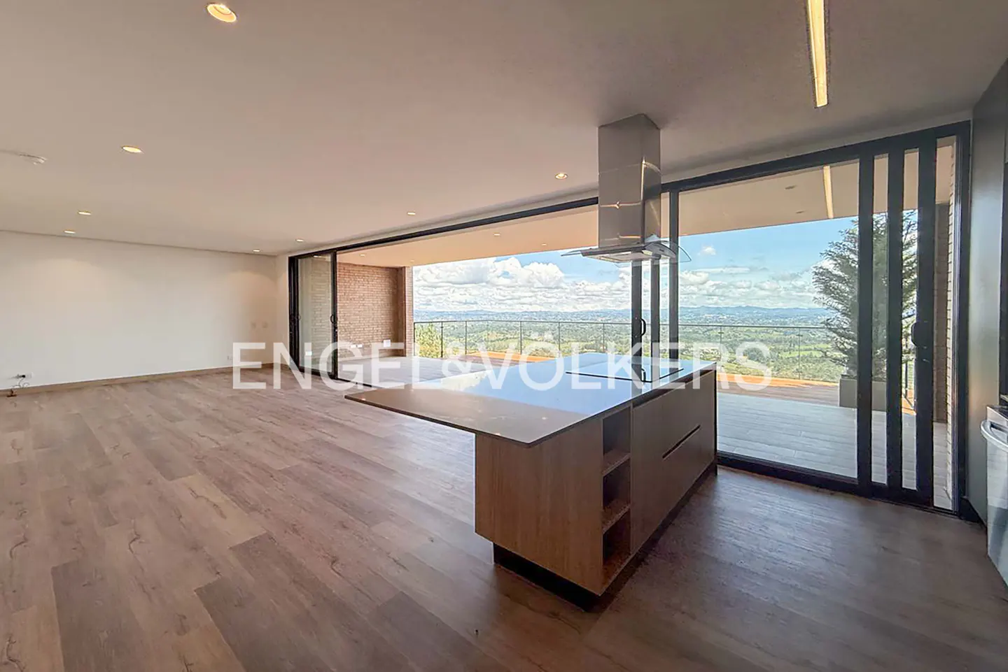 A bright, modern kitchen with wood floors, a large island, and sliding glass doors leading to a balcony with a scenic view.