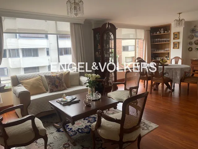 A living and dining room with hardwood floors, a sofa, chairs, a table, and a bookcase.