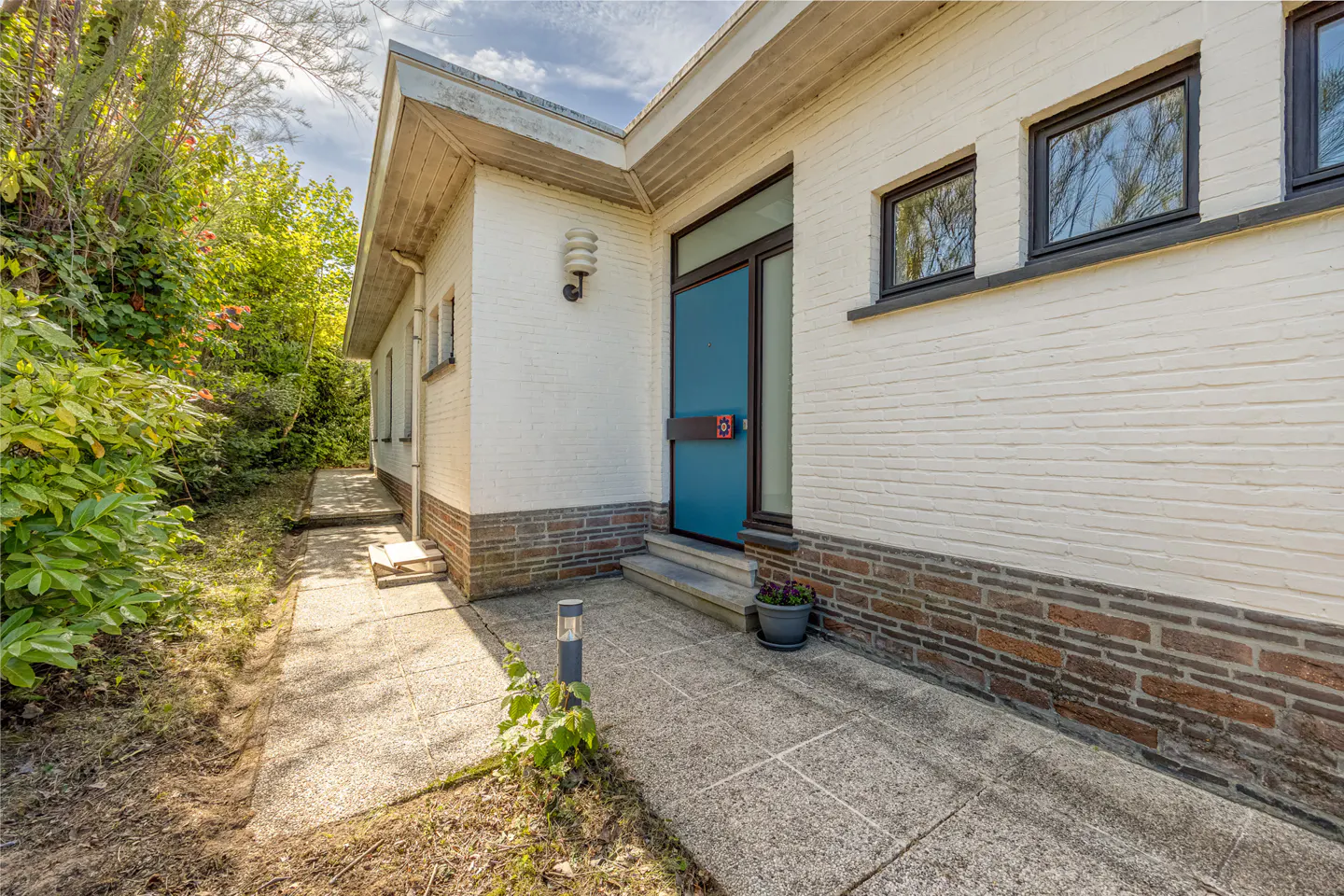 Exterior of a white brick house with a blue door and a concrete walkway leading to the entrance.