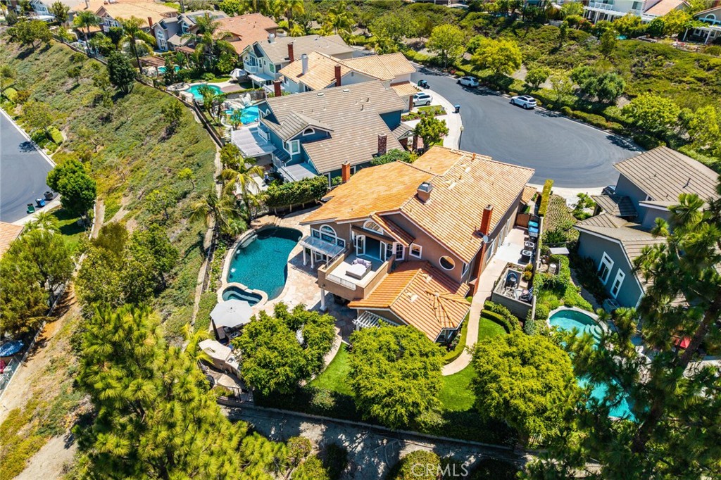 Aerial view of a suburban hillside neighborhood featuring homes with terracotta roofs, private pools, and lush landscaping.