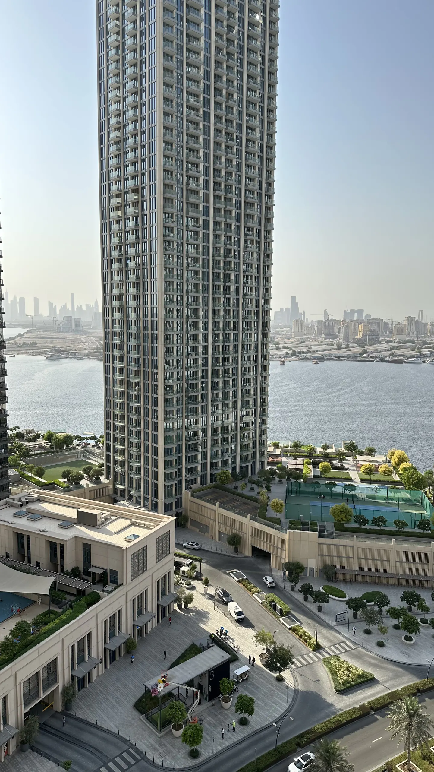 View of a tall, modern apartment building with balconies, overlooking a bay and city skyline.
