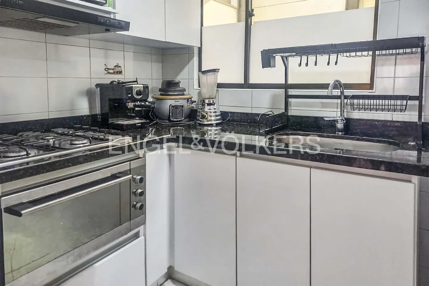 A kitchen with white cabinets, black granite countertops, and stainless steel appliances. A sink and dish rack are visible.
