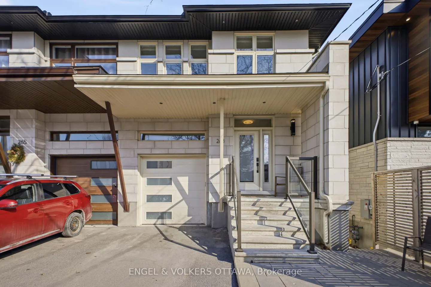 Exterior of a two-story stone house with a white door, garage, and a red car parked in the driveway.