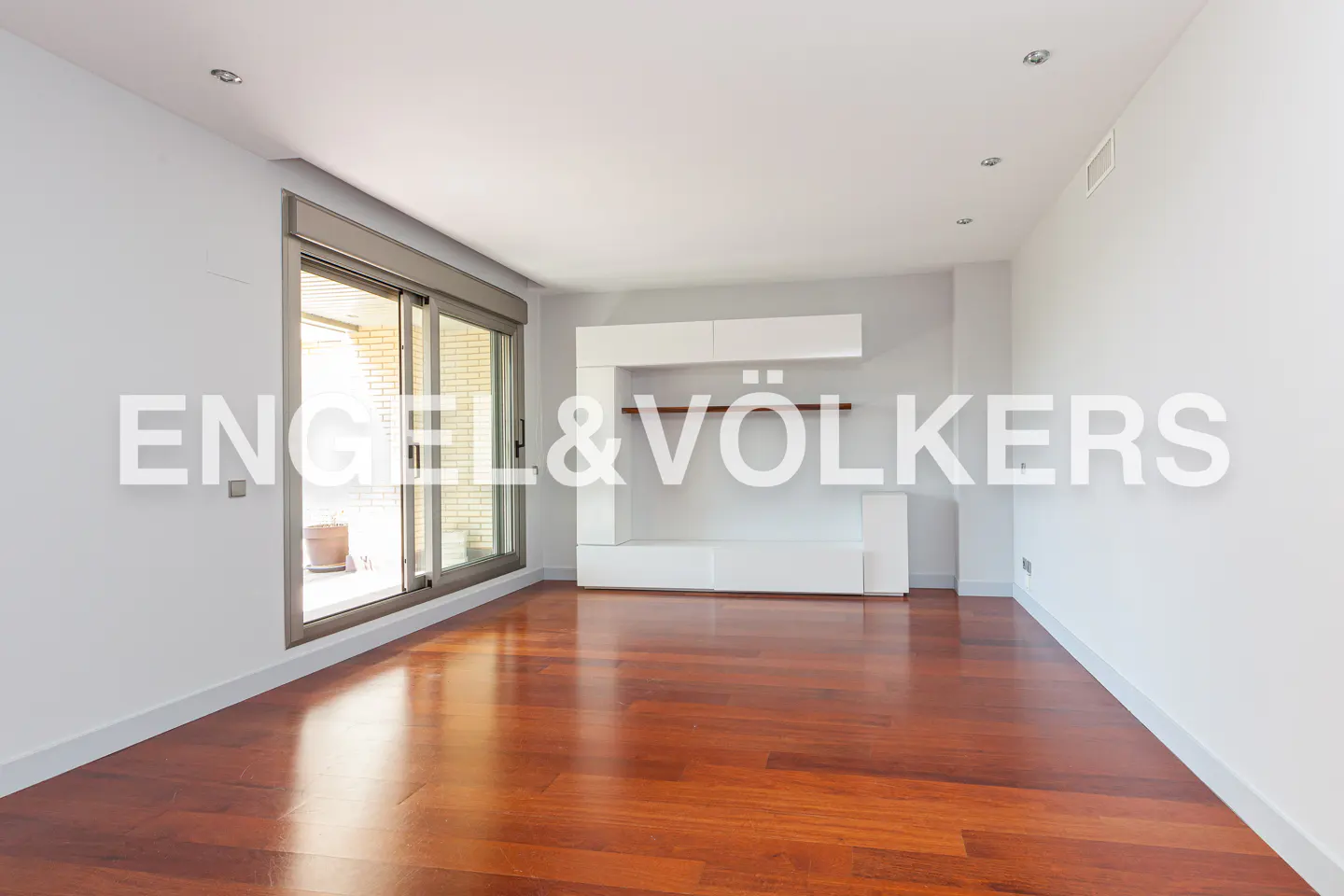 Empty room with hardwood floors, white walls, and a sliding glass door to a balcony. White shelving unit on the back wall.