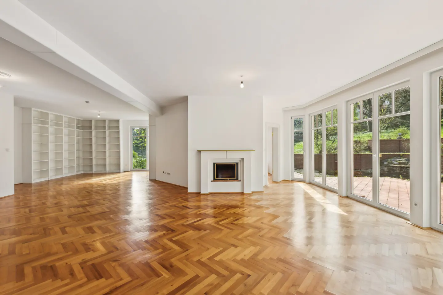 Spacious living room with herringbone wood floors, a white fireplace, built-in shelving, and large windows to a patio.