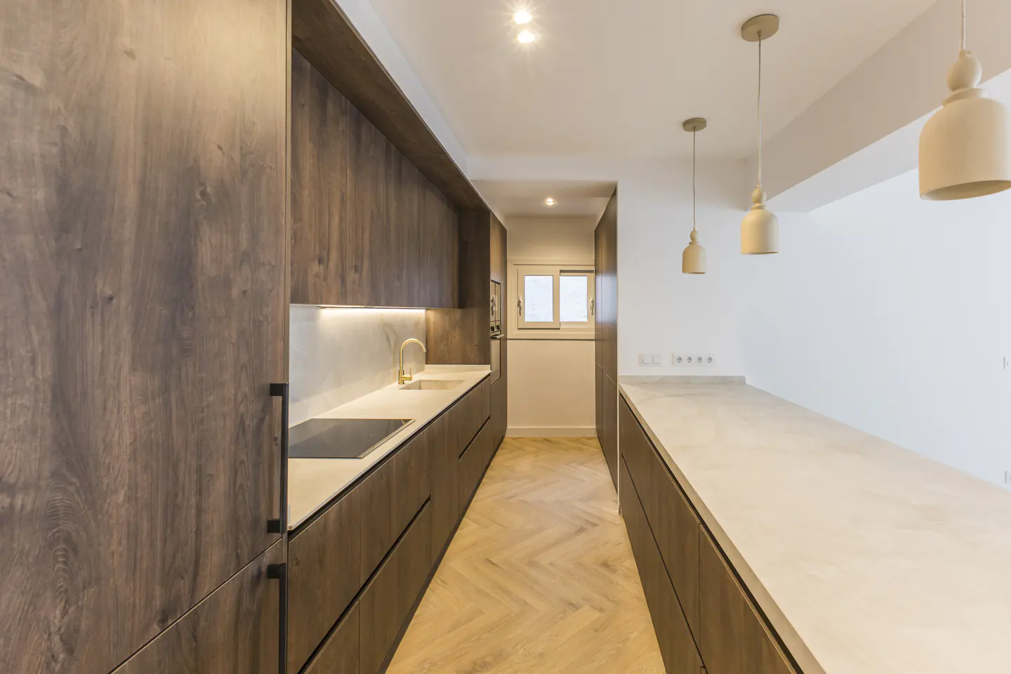 A modern kitchen with wood cabinets, white countertops, and pendant lights. A window is visible in the background.