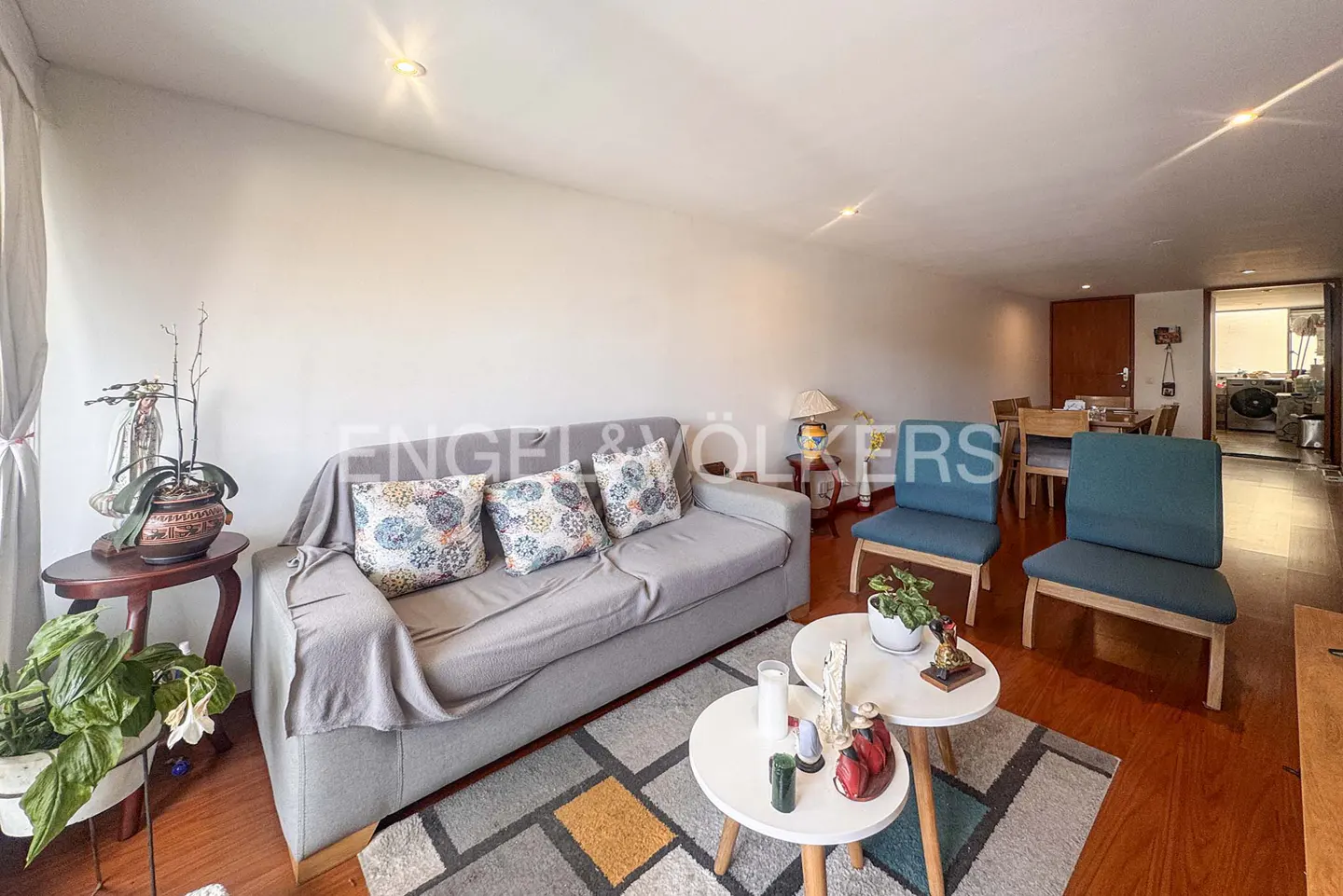 Living room with a gray sofa, patterned pillows, two blue chairs, and two white round tables on a geometric rug.