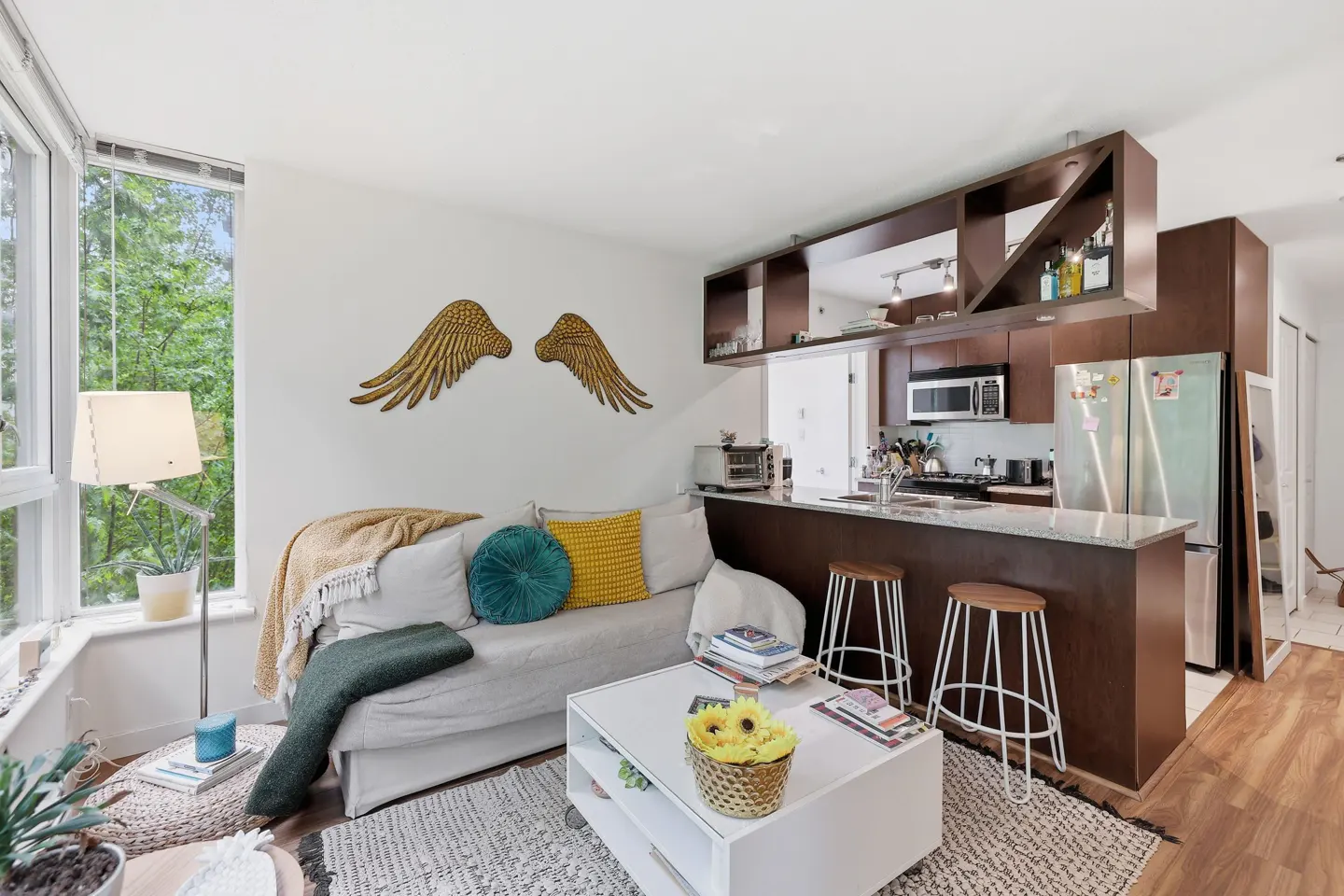 Bright apartment interior with a white sofa, kitchen bar with stools, and gold wing wall decor.