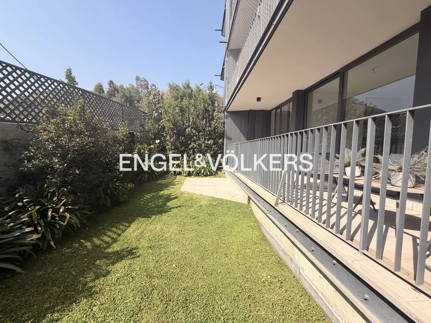 A modern building with a gray balcony overlooks a green lawn and garden. The Engel & Völkers logo is superimposed on the image.