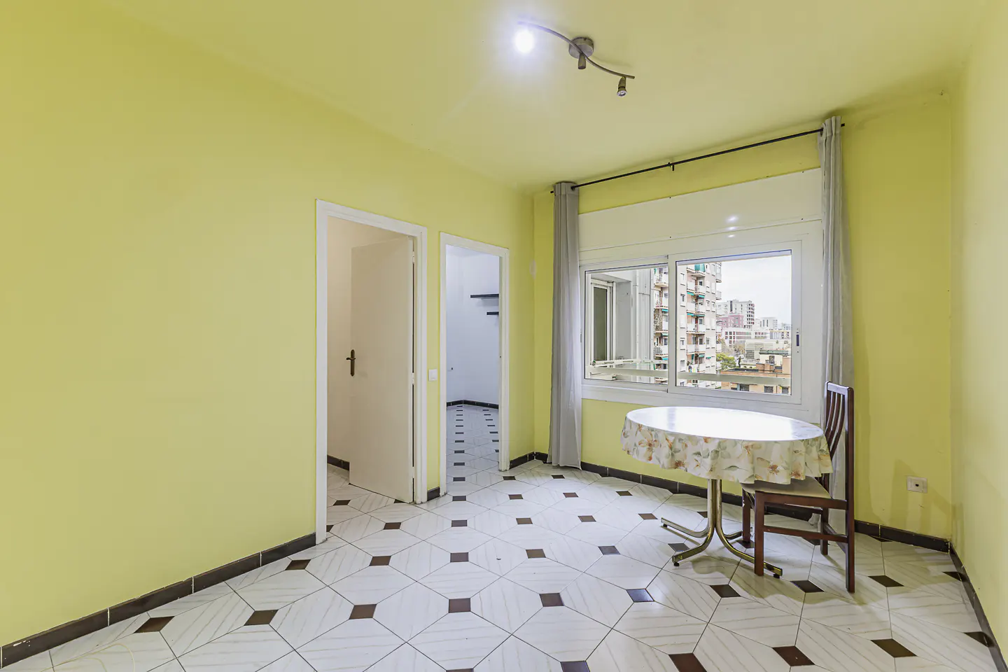 A bright yellow room with a table, chair, and a view of city buildings.