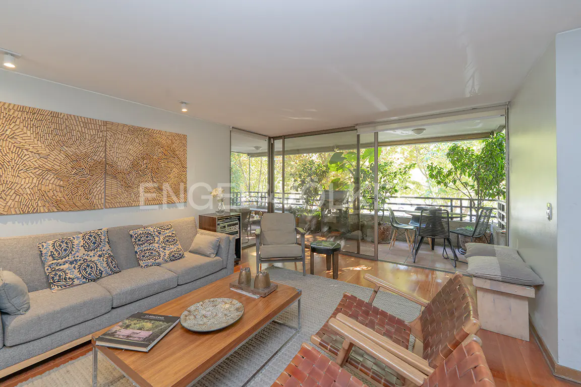 A bright living room with a gray sofa, wood coffee table, and a balcony with green trees.