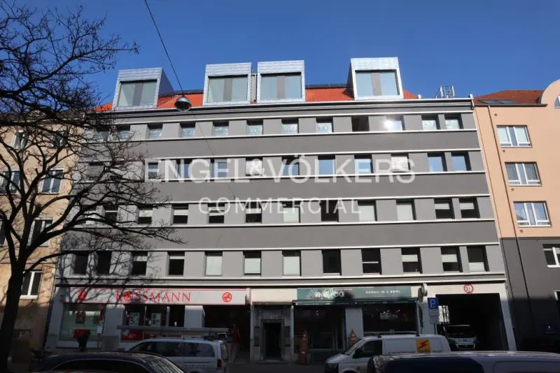 Exterior of a gray commercial building with shops on the ground floor under a blue sky. "Engel & Volkers Commercial" is printed on the building.