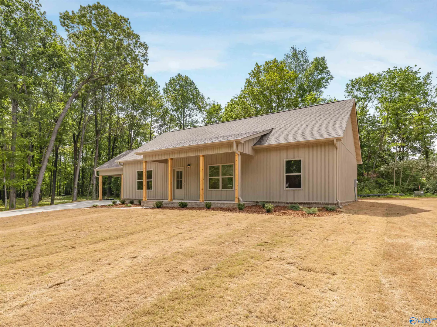 A beige single-story house with a covered porch and a carport, surrounded by trees and a dry lawn.