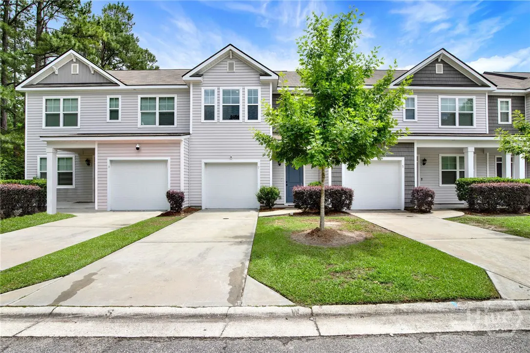 Three light gray townhouses with white garage doors and concrete driveways under a blue sky.
