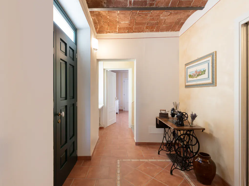Hallway with terracotta tile floor and brick ceiling. A black door is on the left, and a vintage sewing machine is on the right.