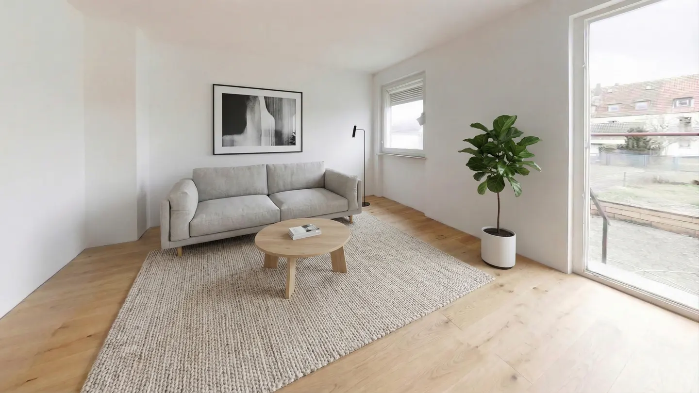 Bright living room with a gray sofa, round wood table, and a large window overlooking a yard. A black and white art piece hangs above the sofa.